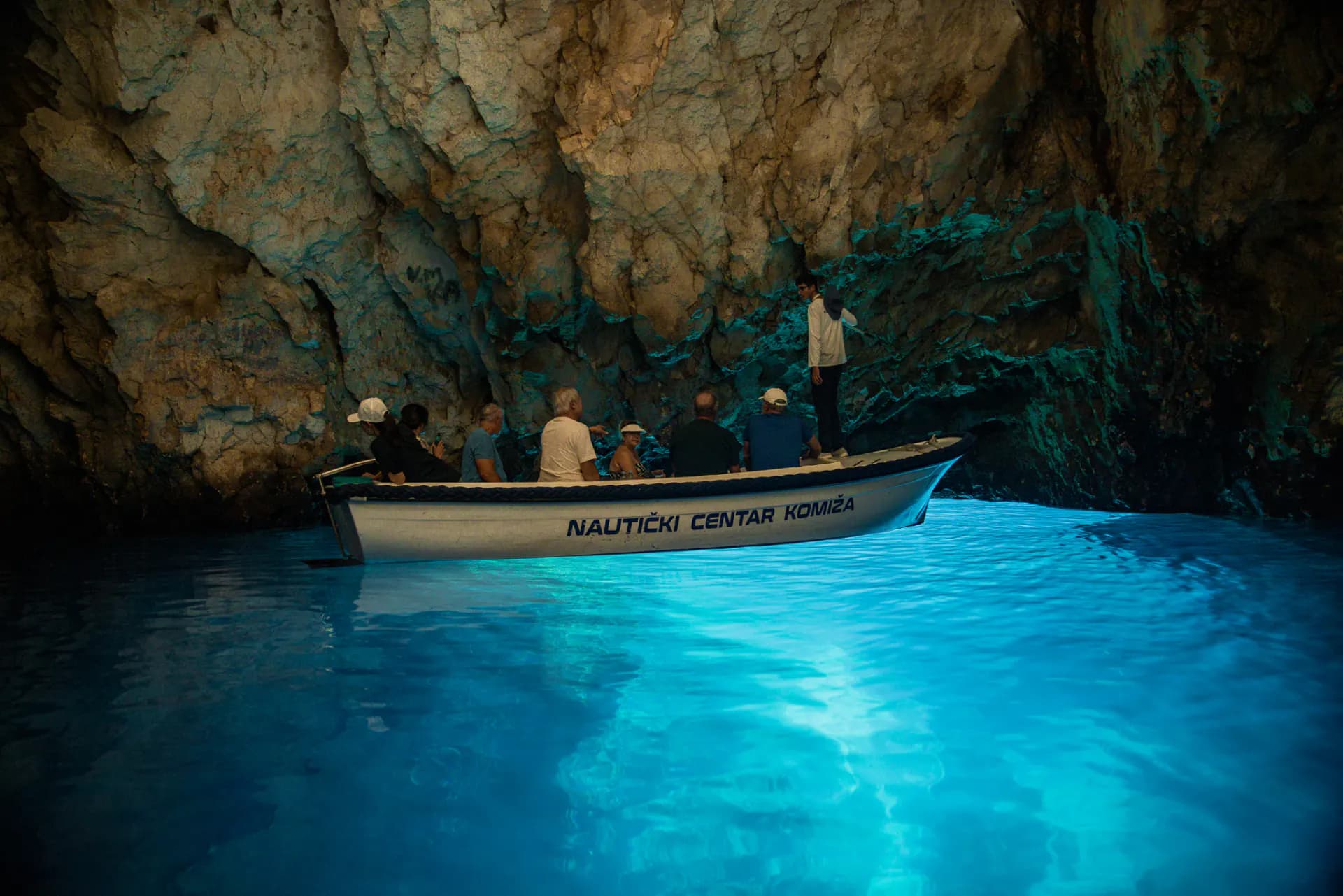 The local wooden barque inside the Blue Cave, the water lit electric blue beneath it — Blue Cave & 5 Islands — Private