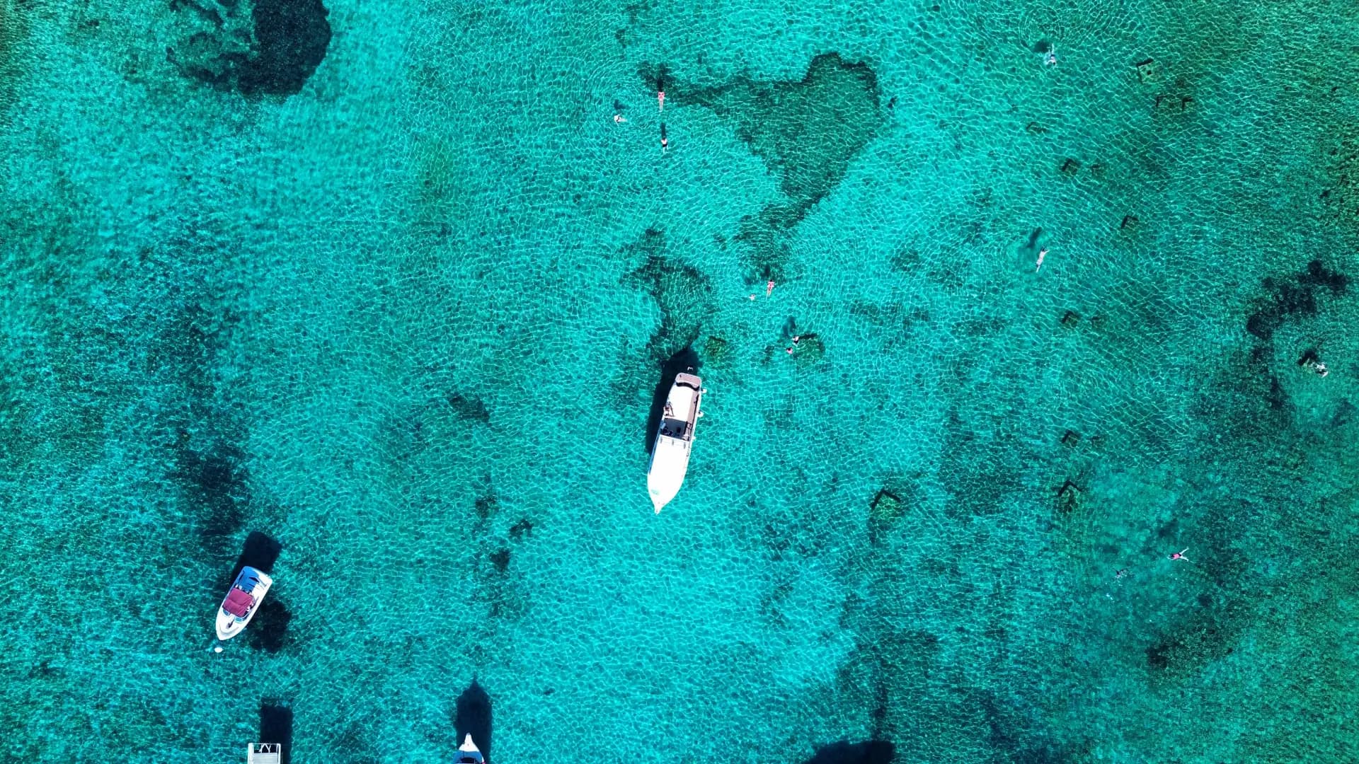 The Blue Lagoon straight down from above, boats at anchor and swimmers scattered across water shallow enough to see the seabed. Blue Lagoon & Trogir: Private Half Day