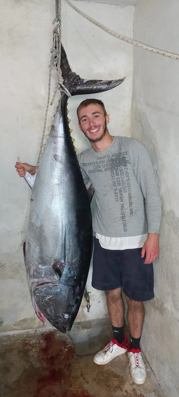 Tino next to a bluefin tuna nearly his own height, hung up after a winter fishing trip. Blue Cave Tours